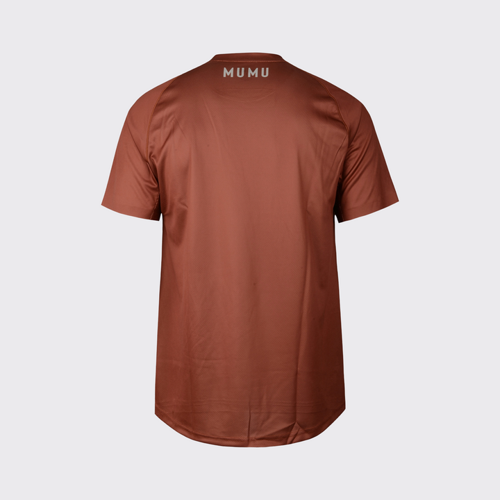 Rust brown short-sleeve MTB jersey shown from the back, featuring a relaxed fit, subtle textured performance fabric, slightly extended rear hem, and light MUMU branding centered below the collar, shown against a light gray background.

